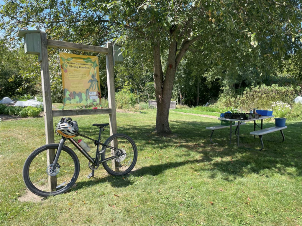 A bike leans against the sign for the Orono Community Giving Garden, at the garden's entrance.